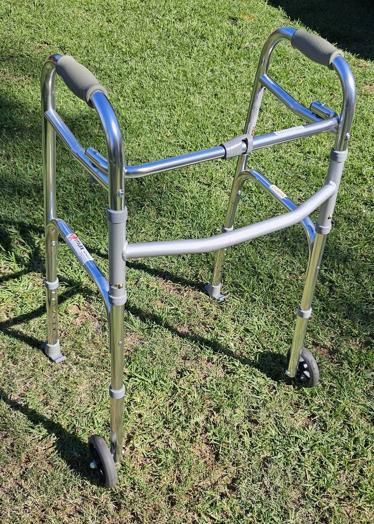Lightweight metal walker with two front wheels and padded hand grips, photographed outdoors to show frame condition