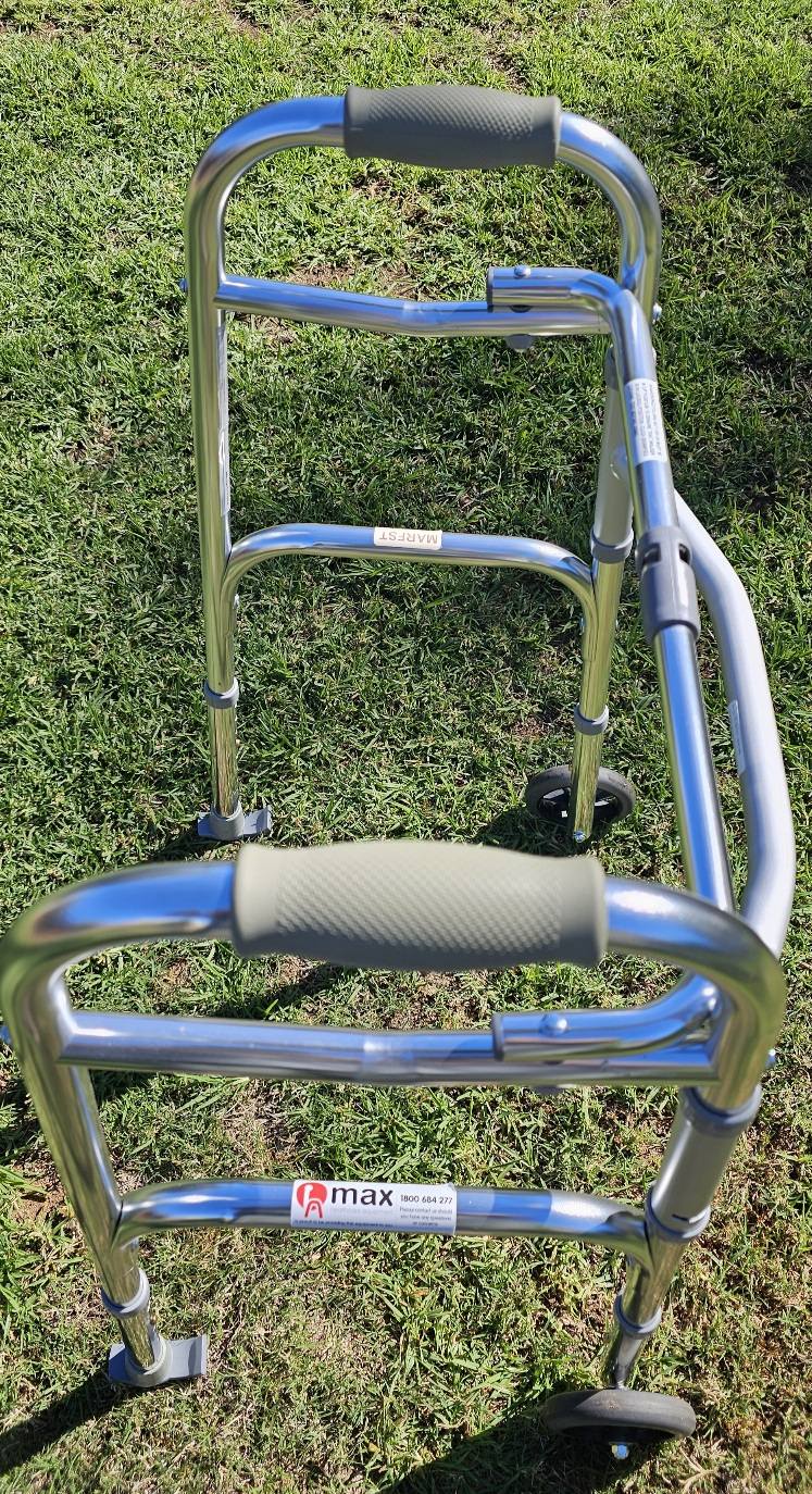 Aluminium walker with two front wheels, padded hand grips and rear stoppers, photographed outdoors to show frame condition