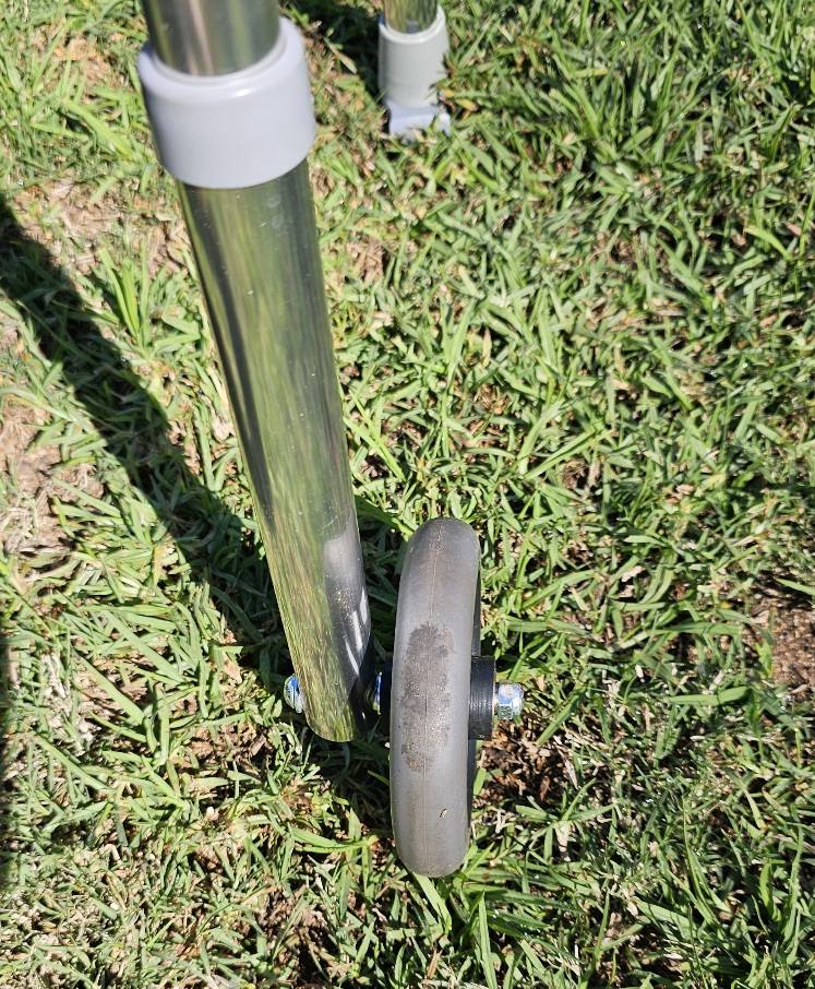 Close‑up of a walker’s front wheel and aluminium leg, photographed outdoors to show condition and wear details