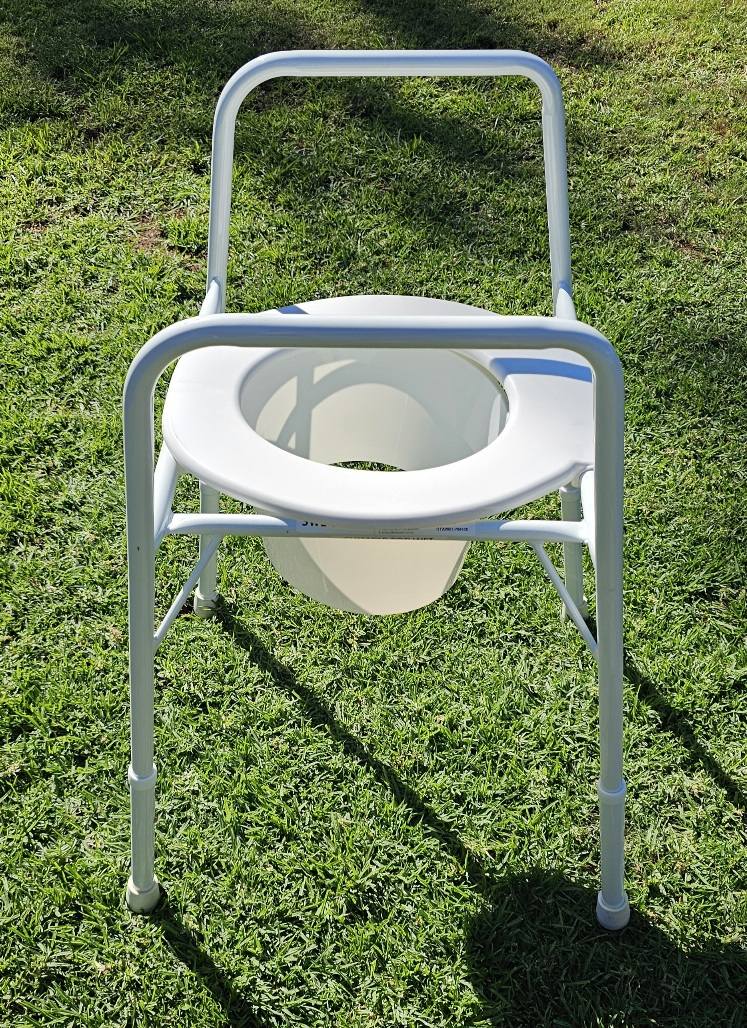 White commode chair with metal frame and removable bucket, photographed outdoors to show overall structure and condition