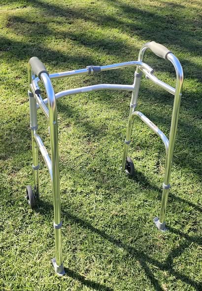Lightweight metal walker with two front wheels and padded handles, photographed outdoors to show frame condition