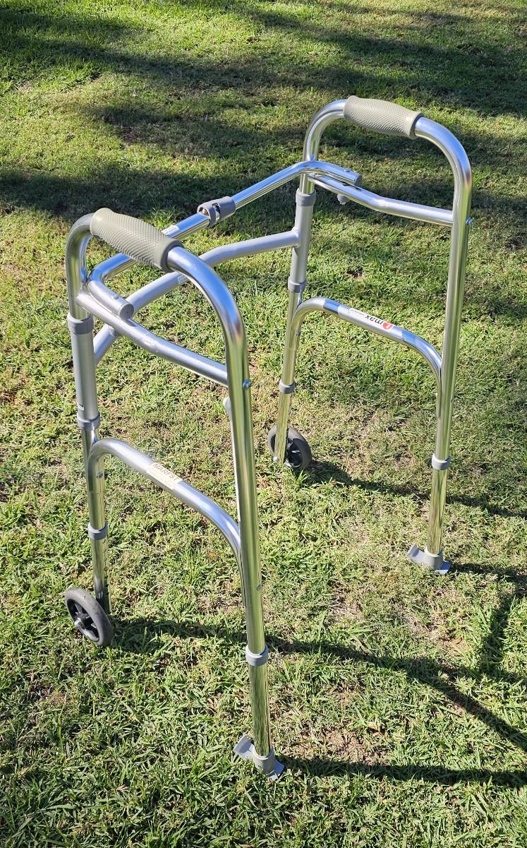 Metal walker with two front wheels and padded hand grips, photographed outdoors to show frame condition and stability features