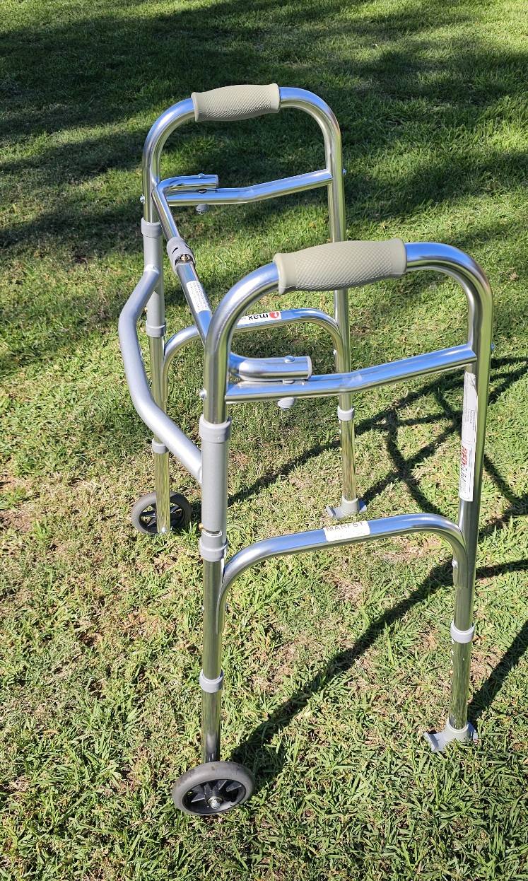 Metal walker with two front wheels and padded hand grips, photographed outdoors to show frame condition and support features